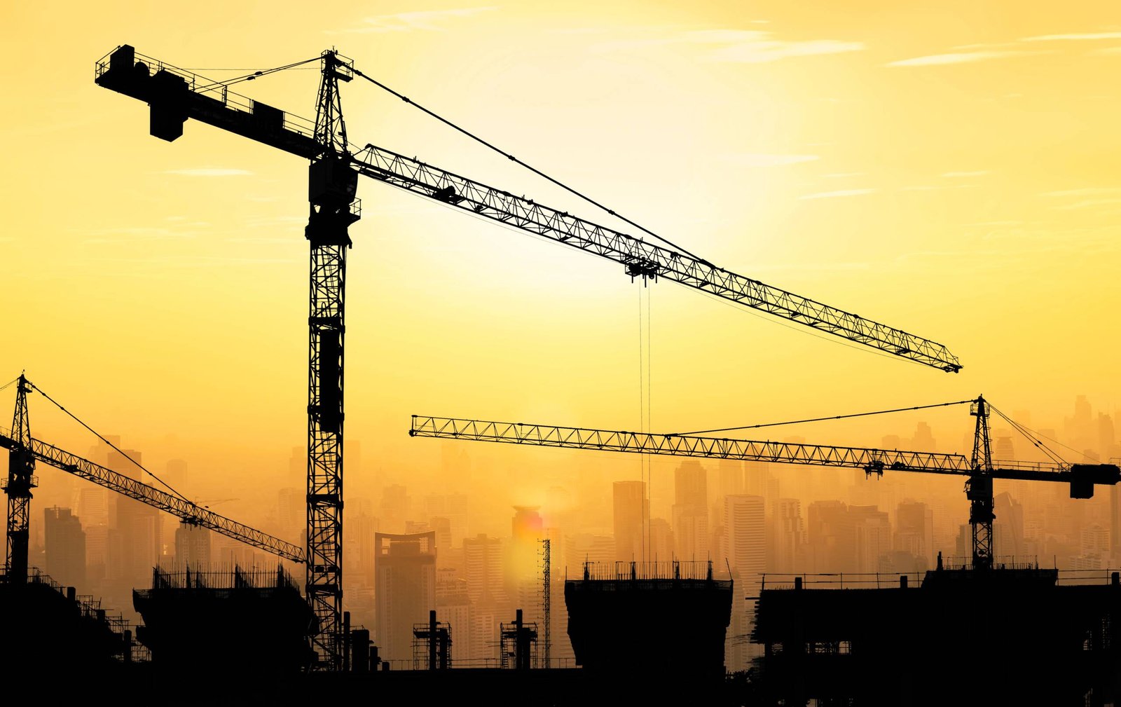 Big cranes and building construction against beautiful dusky sunset sky with cityscape in background.